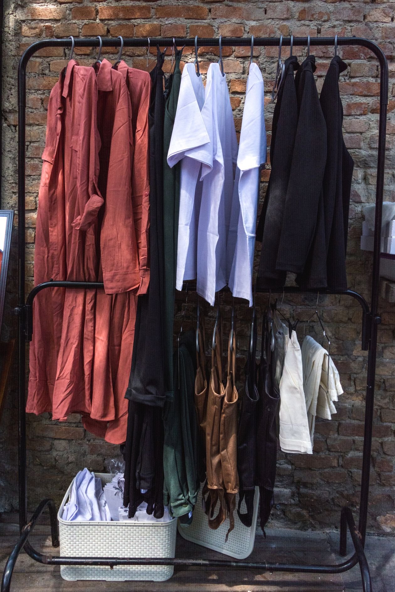 A rack of colorful clothing on hangers against a brick wall