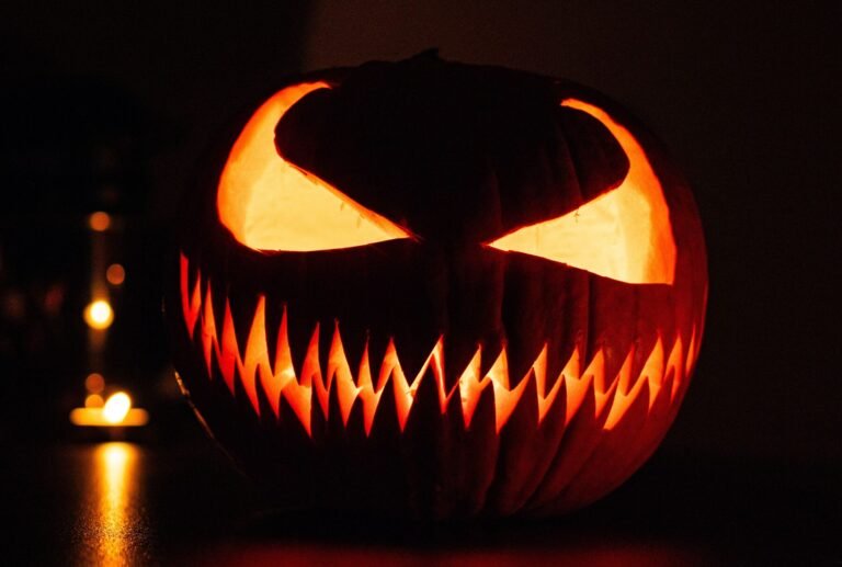 A carved jack-o'-lantern glowing in the dark next to a lit candle
