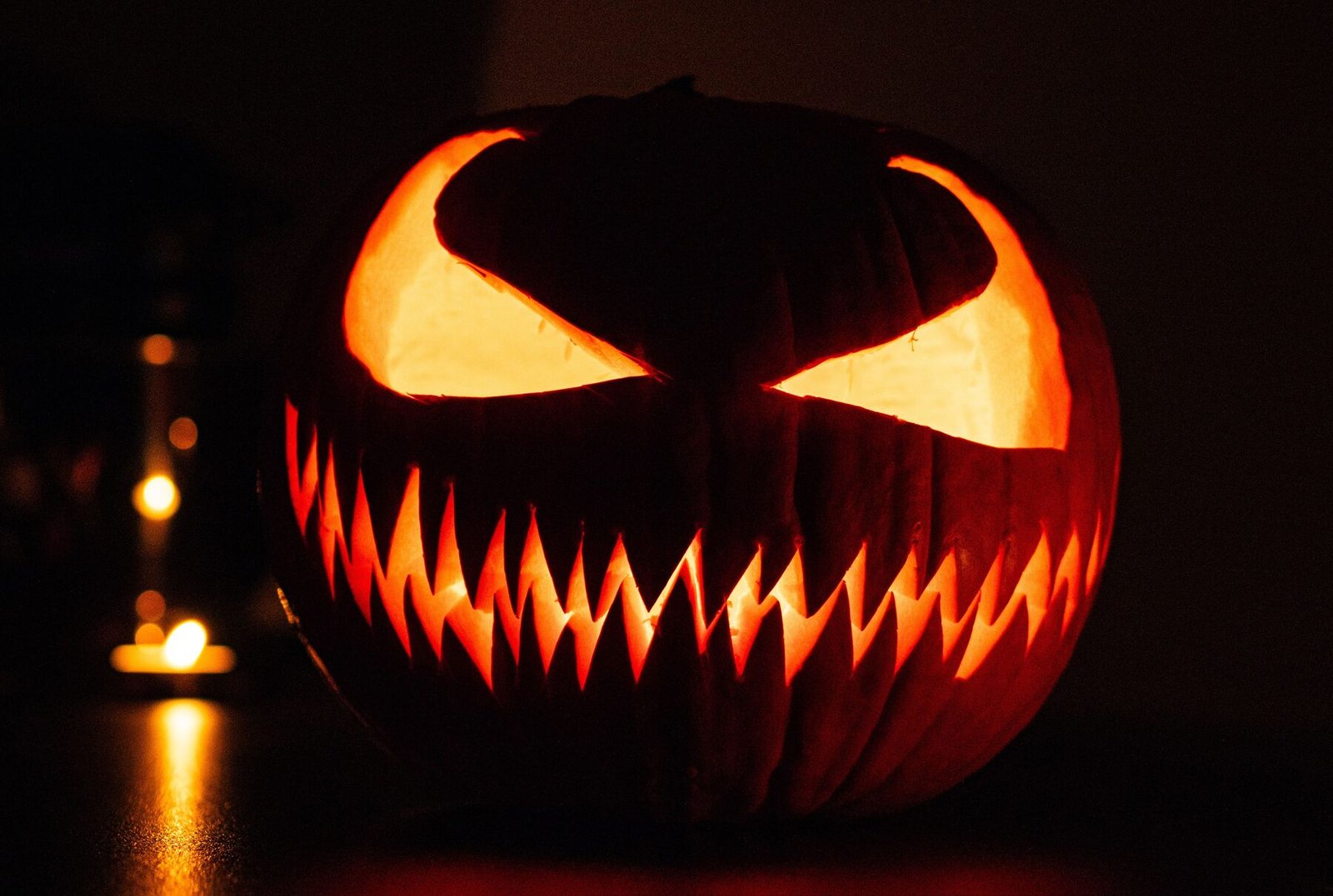 A carved jack-o'-lantern glowing in the dark next to a lit candle